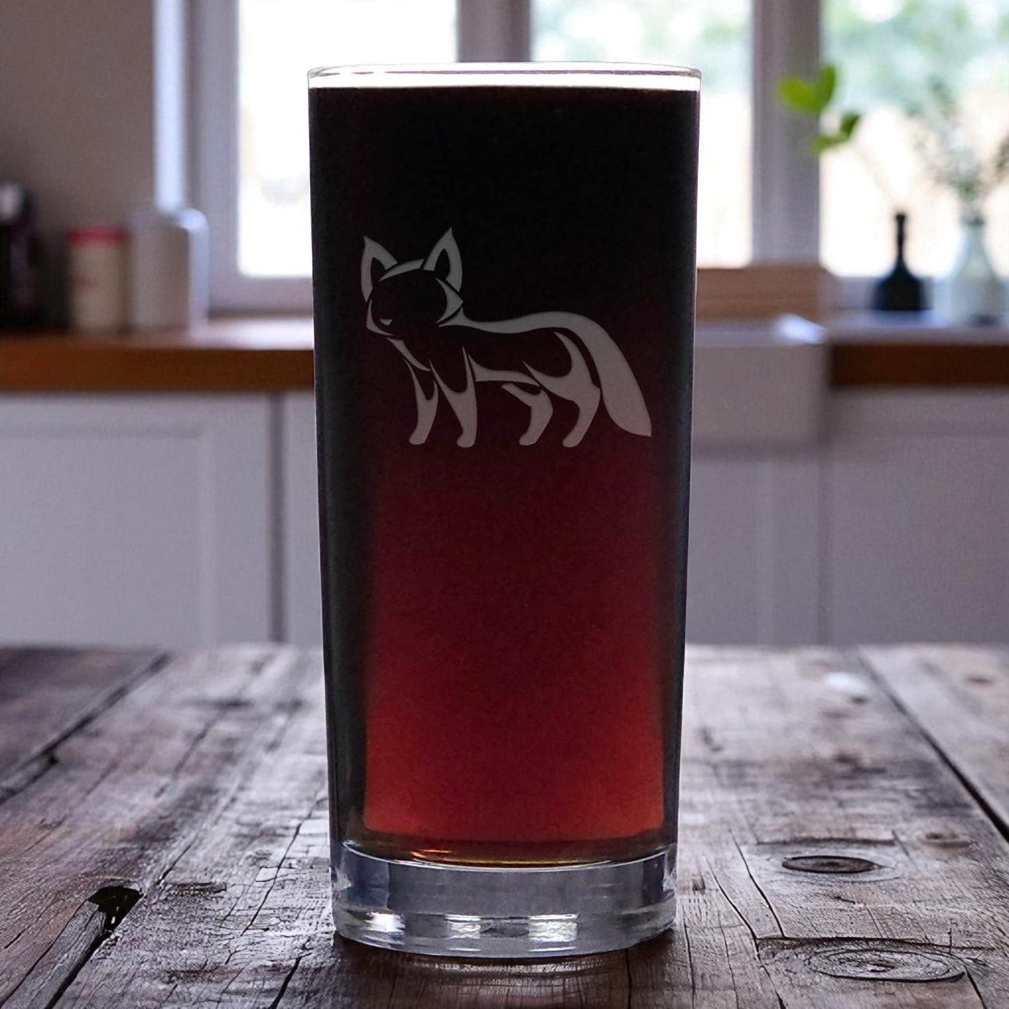 Pint glass with a fox design on a wooden table in a kitchen setting