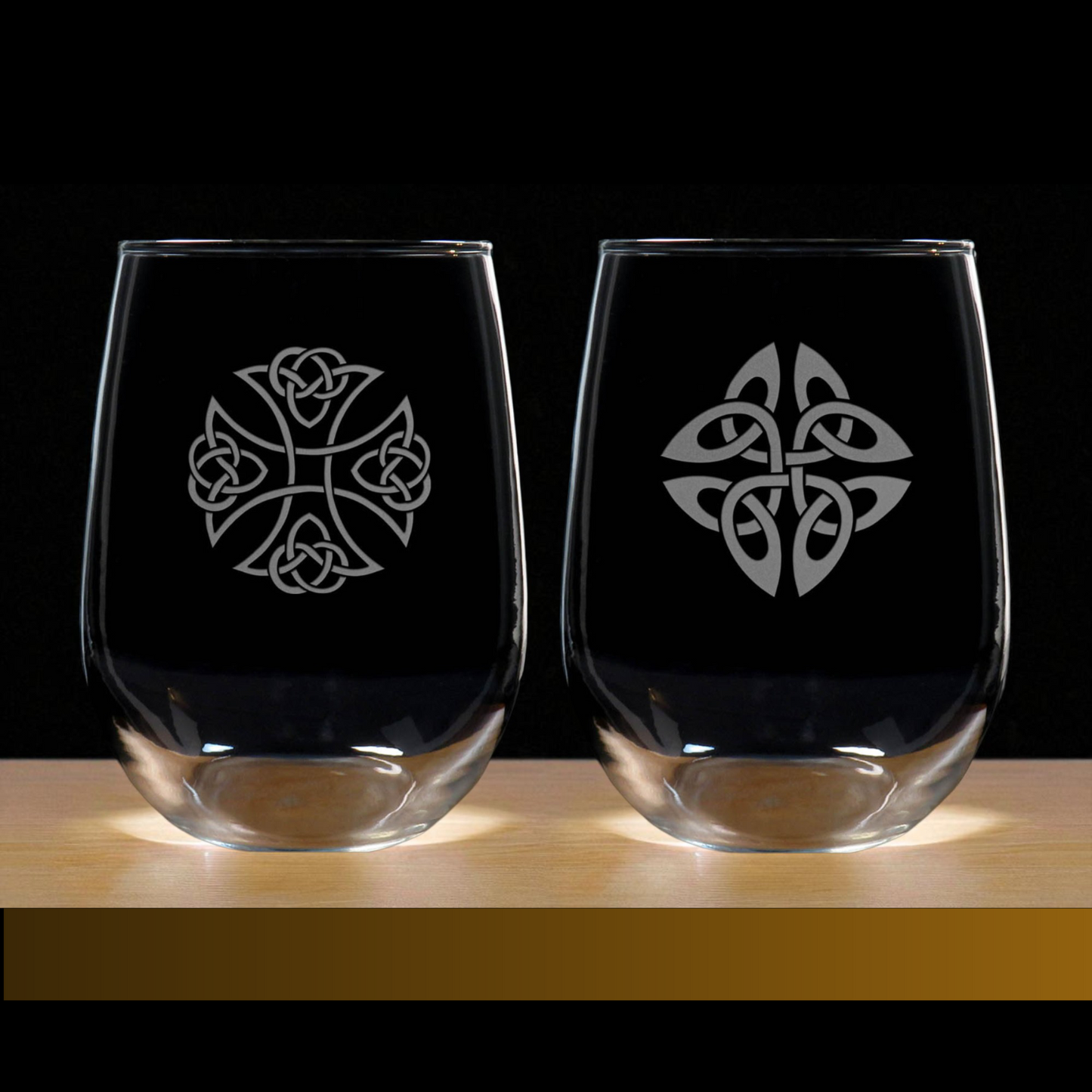 Two clear glasses with Celtic knot designs on a wooden surface and black background