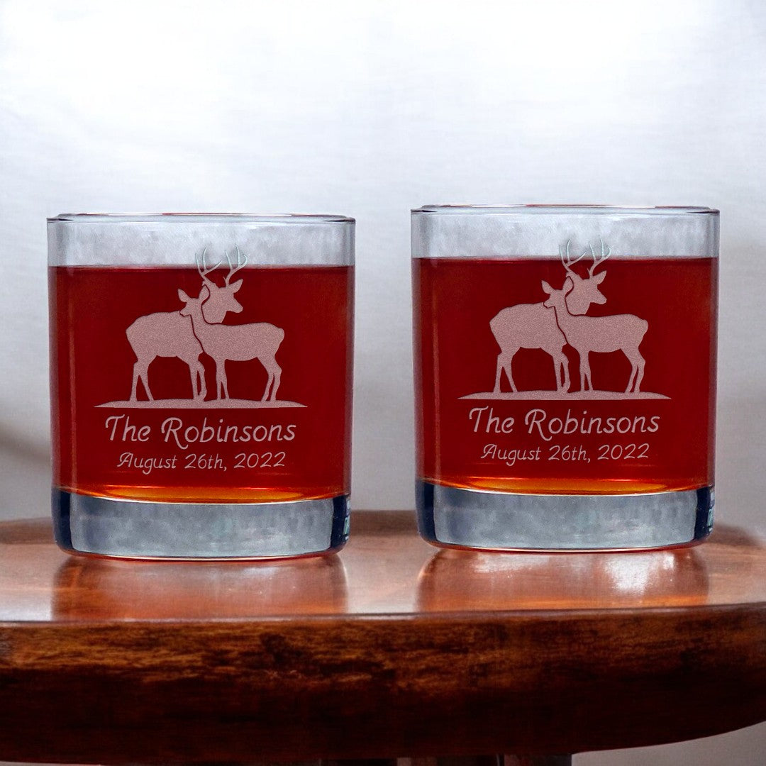 Two glasses with sandblasted stag and doe design and text on a wooden surface