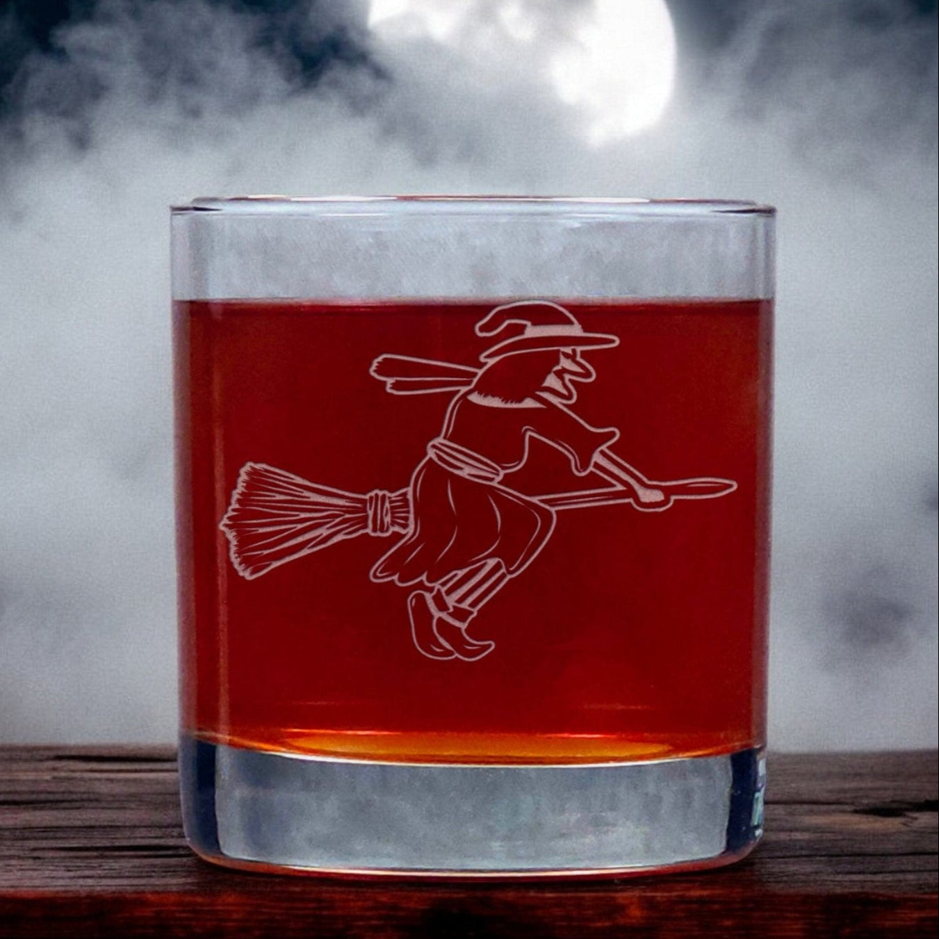 An image of an 11oz whiskey glass with a misty background with a witch on her broomstick.