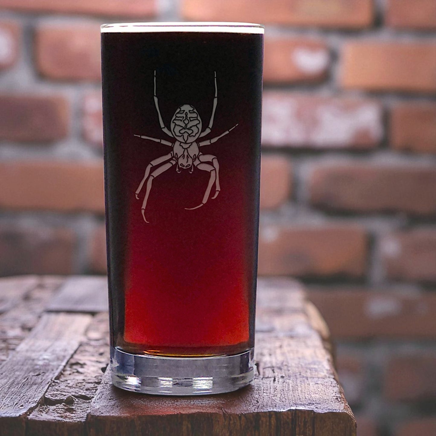 Glass with a spider design filled with red liquid on a wooden surface with a brick wall background