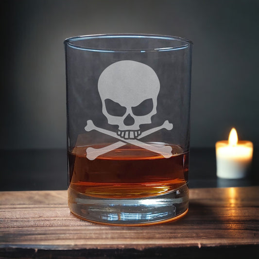 Glass with skull and crossbones design filled with a dark liquid on a wooden surface with a candle in the background.