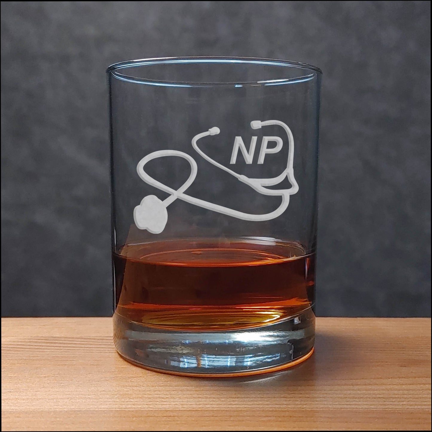 Nurse Practitioner Whiskey Glass with a etched image of a Stethoscope and the designation letters N P on  it - Copyright Hues in Glass