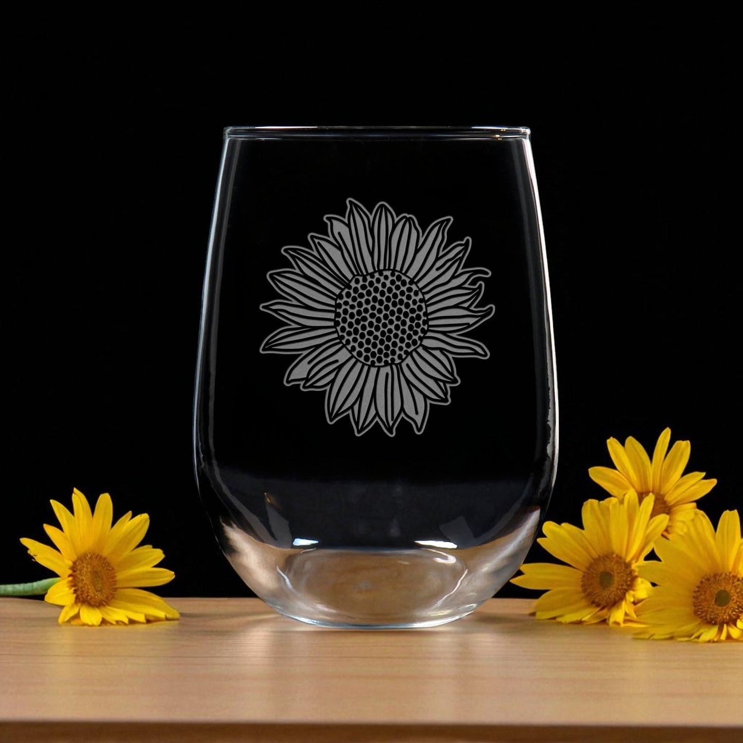 Clear glass with sunflower design on a wooden surface with yellow flowers.