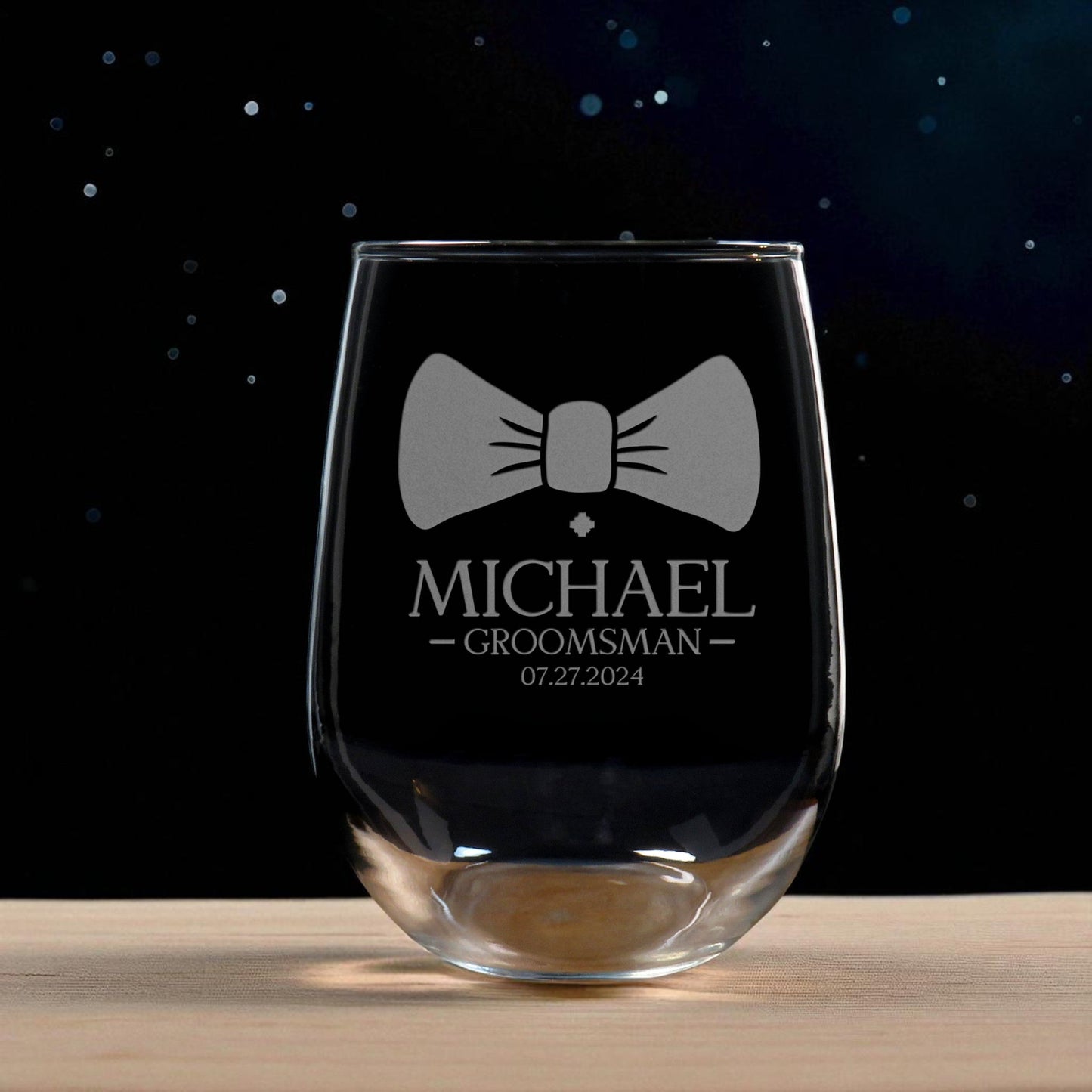 Clear glass wine glass with engraved bow tie design and text on a dark background