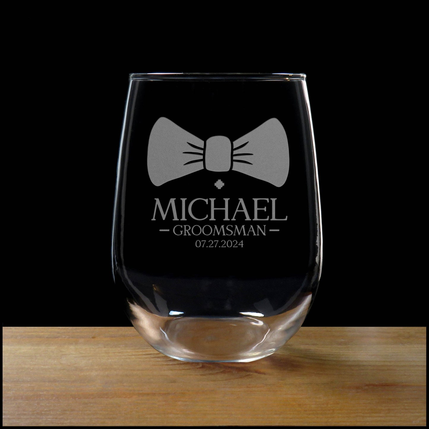 Clear glass with bow tie design and engraved text on a wooden surface with black background