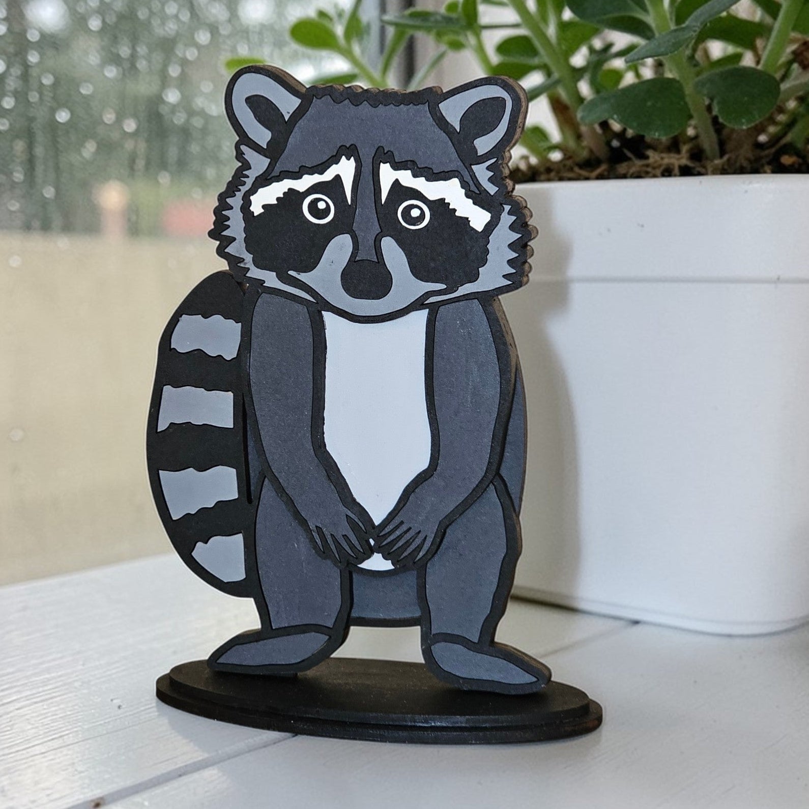 DIY Raccoon paintable shelf sitter kit on a white surface with a blurred outdoor background