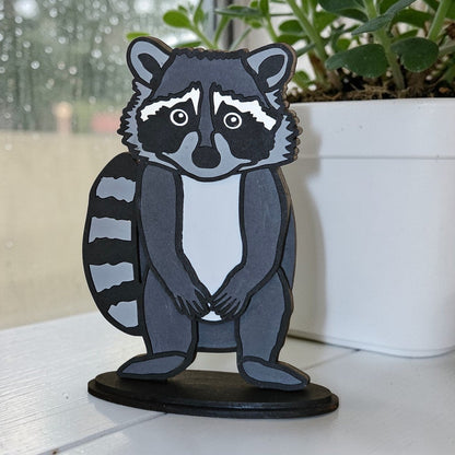 DIY Raccoon paintable shelf sitter kit on a white surface with a blurred outdoor background