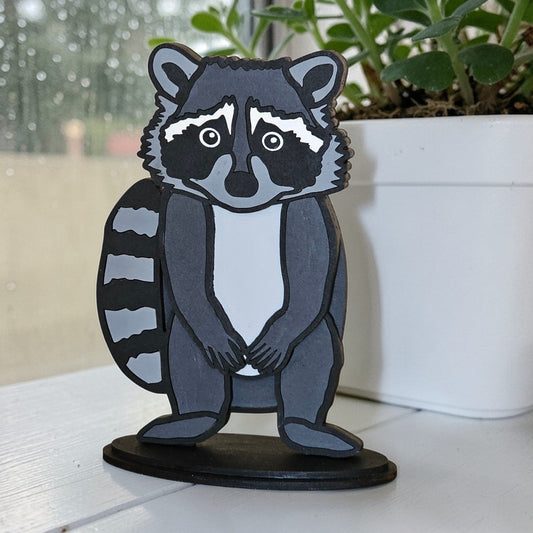 DIY Raccoon paintable shelf sitter kit on a white surface with a blurred outdoor background