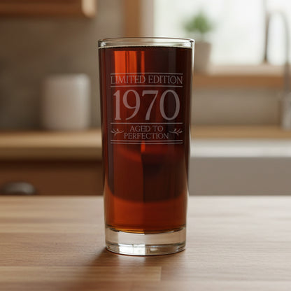 Glass with 'Limited Edition 1970 Aged to Perfection' text on a wooden counter with a minimal kitchen in the background