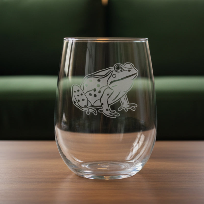 17oz Stemless Wine Glass with an etched image of a garden frog 
and a green couch in the background