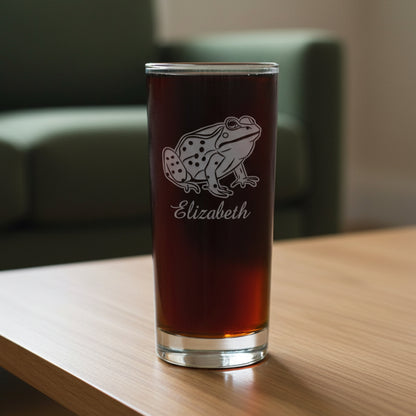 15oz Cooler Glass with an etched image of a climbing frog on a wood table and a green couch in the background