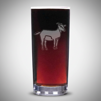 A clear glass shot glass featuring a white etched silhouette of a goat, shown filled with a dark red liquid against a plain light grey background.