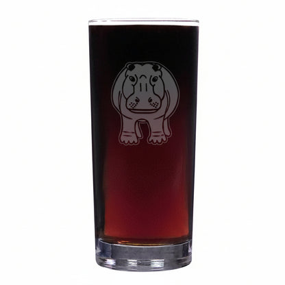 A tall, clear cooler glass filled with dark beer, featuring an etched hippopotamus design on the front, set against a textured white background.