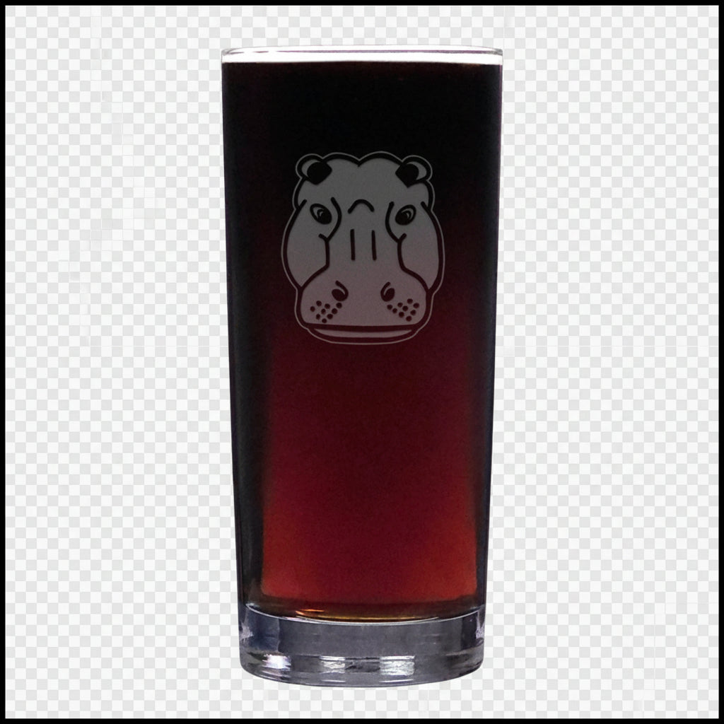 A tall cooler glass filled with dark beer, featuring an etched hippopotamus face design on the front, set against a textured white background.