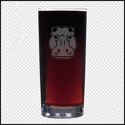 A tall cooler glass filled with dark beer, featuring an etched hippopotamus face design on the front, set against a textured white background.