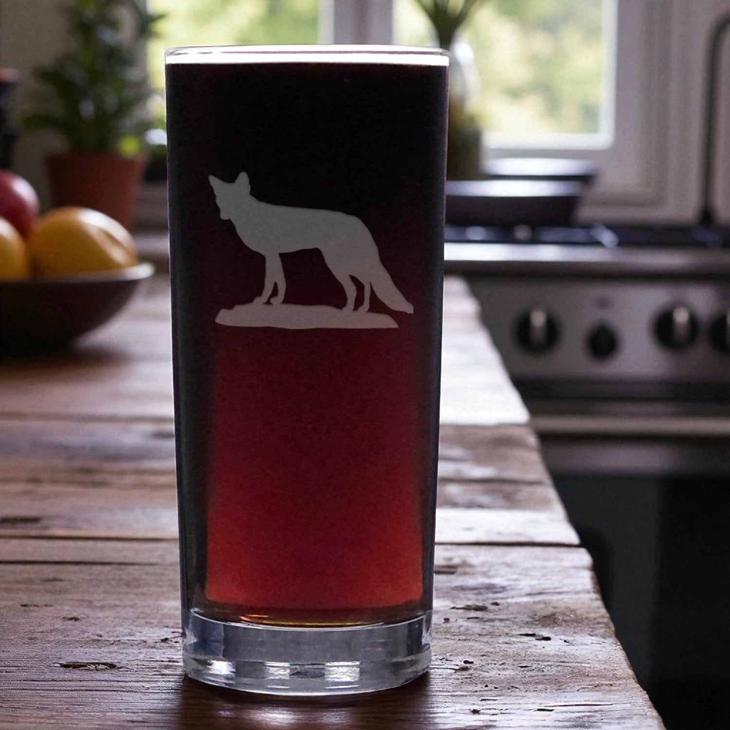 Pint glass with a fox silhouette on a wooden table in a kitchen.