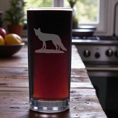 Pint glass with a fox silhouette on a wooden table in a kitchen.