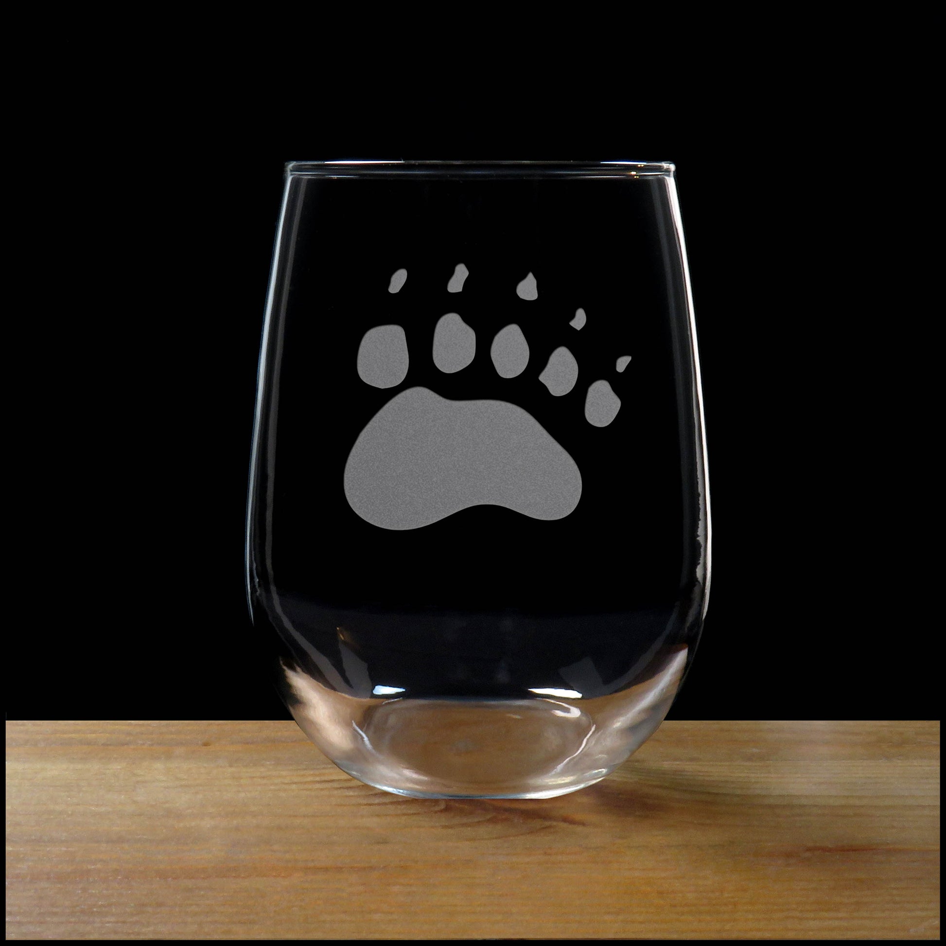 17oz Stemless Wine Glass with an etched image of a bear paw print, on a wood surface and a black background