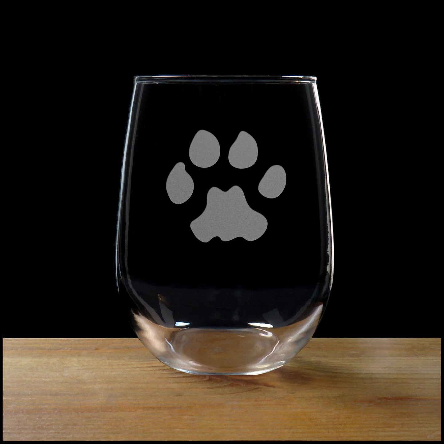 17oz Stemless Wine Glass with an etched image of a cougar paw print, on a wood surface and a black background