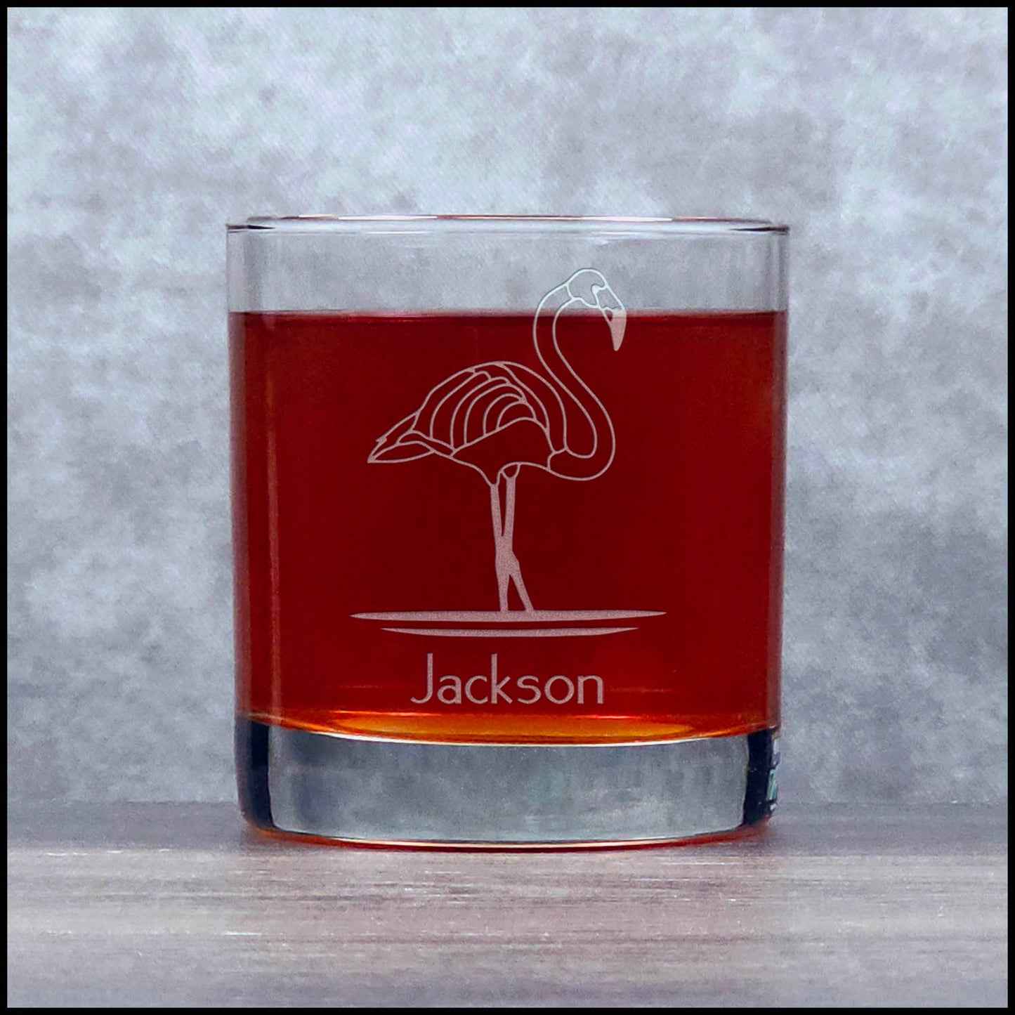 Glass tumbler with flamingo design and 'Jackson' engraving on a gray background