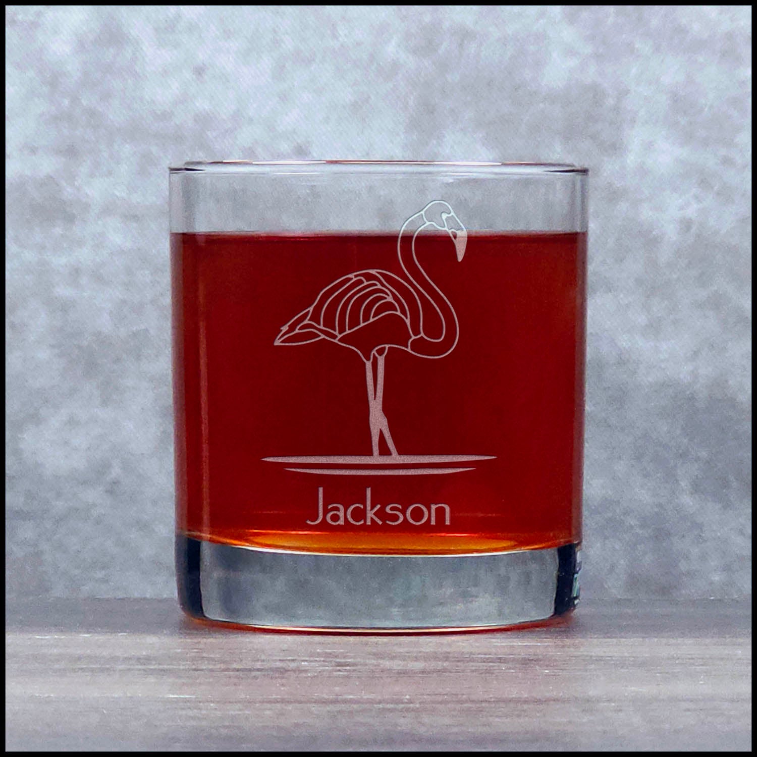 Glass tumbler with flamingo design and 'Jackson' engraving on a gray background