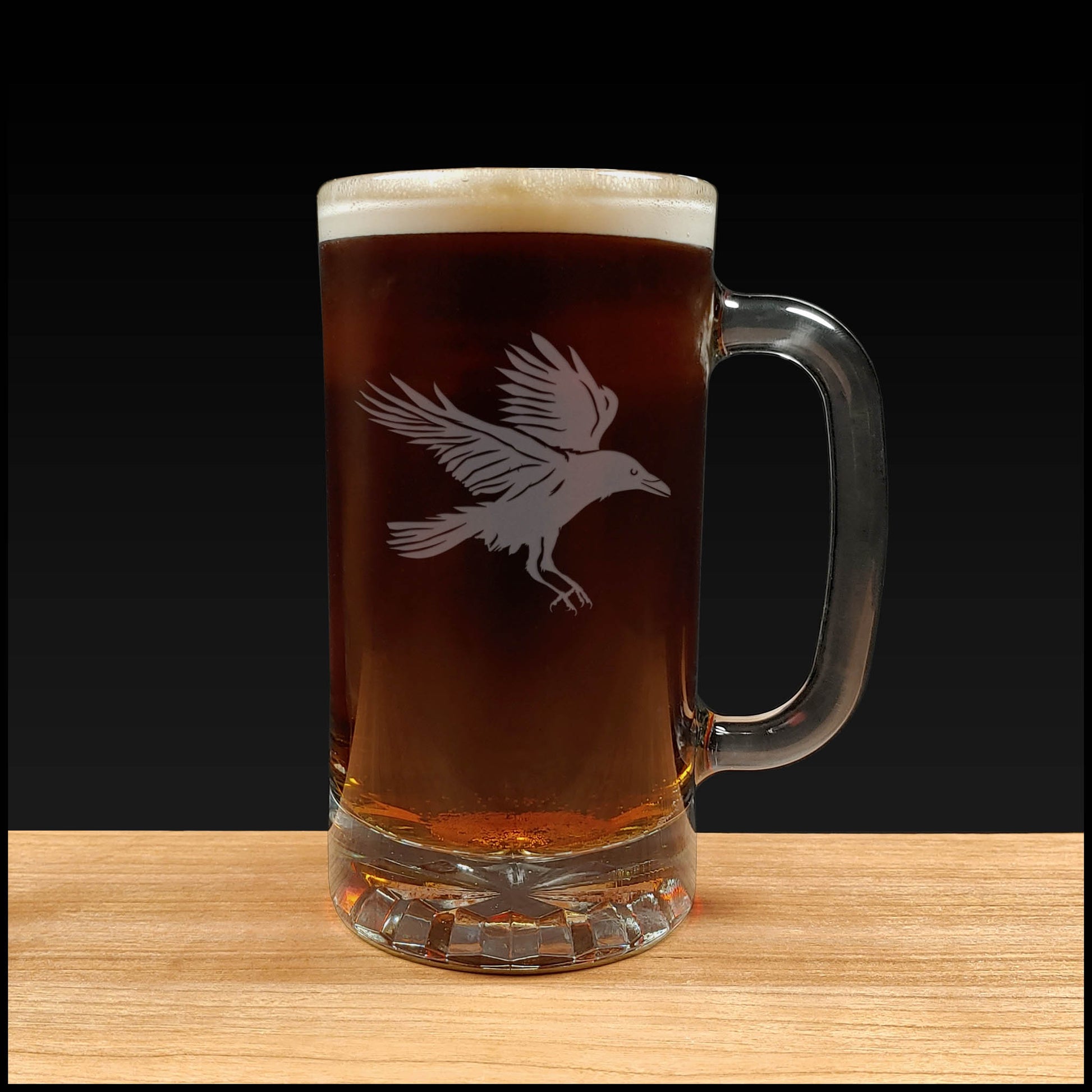 Glass mug with beer and a bird etching on a wooden surface and black background