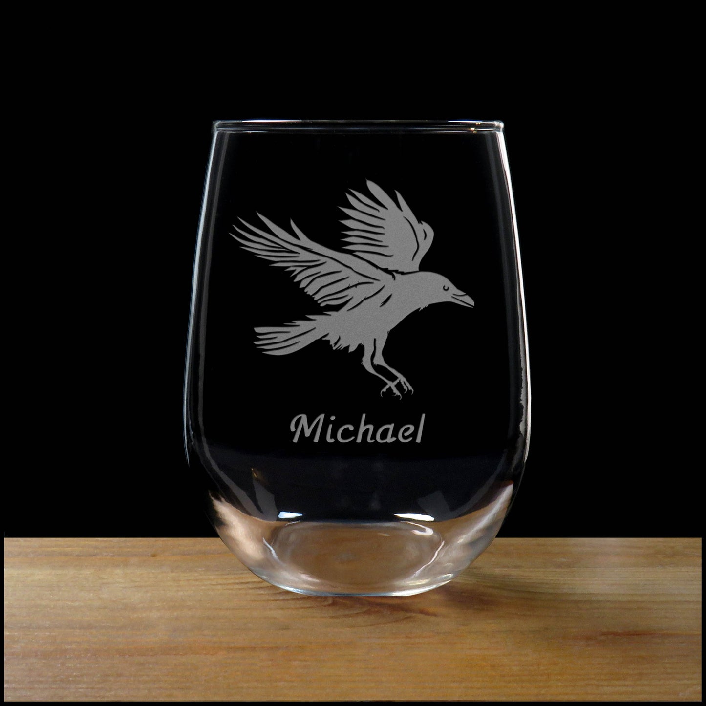 Clear glass with engraved bird design and name 'Michael' on a wooden surface with black background