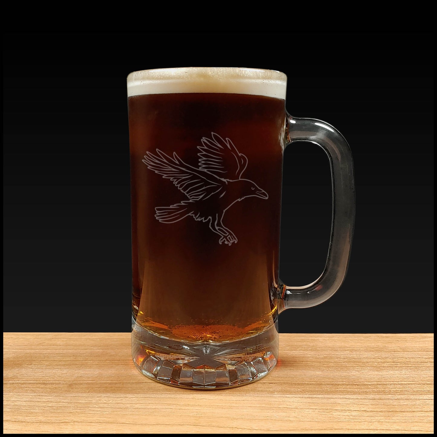 Glass mug with beer and bird engraving on a wooden surface