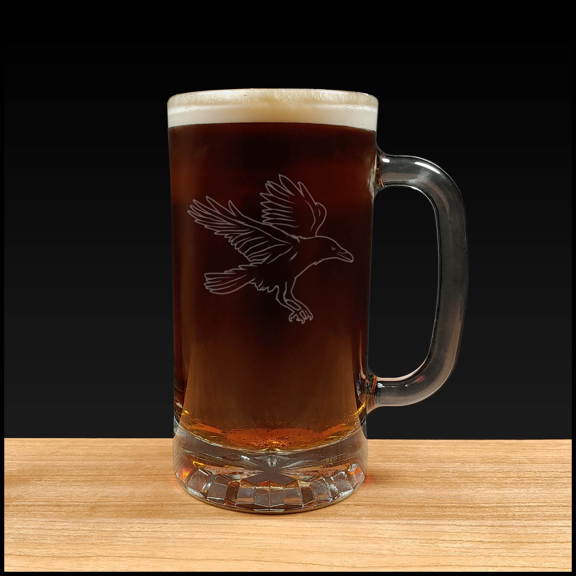 Glass mug with beer and bird engraving on a wooden surface