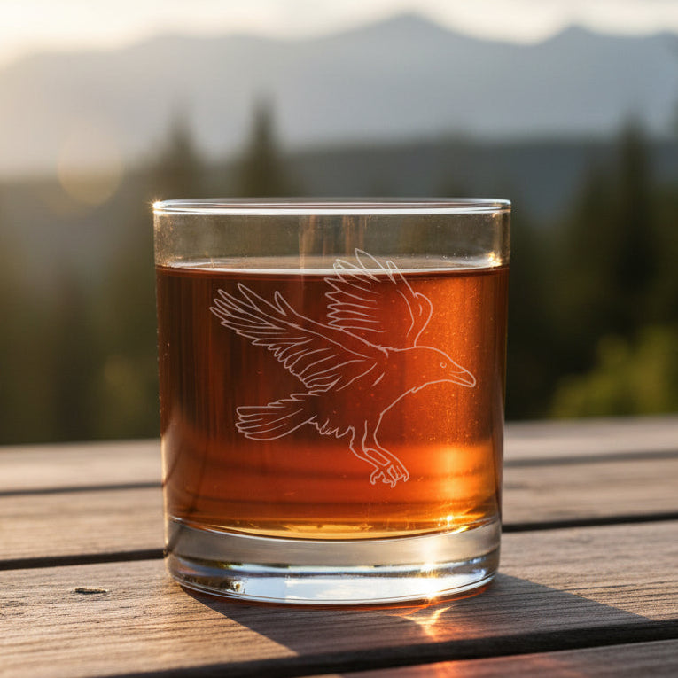 Glass with an Raven etching with a blurred forest in the background