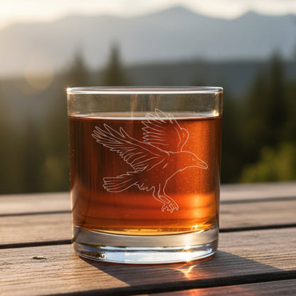 Glass with an Raven etching with a blurred forest in the background