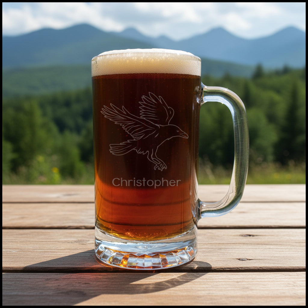 Glass mug with beer and etched raven design on a wooden surface with forest  and mountains in background