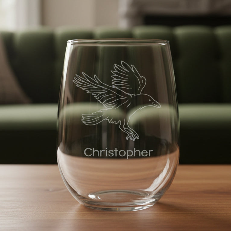 Clear glass stemless wine glass with engraved bird design and 'Christopher' text on a wooden surface.
