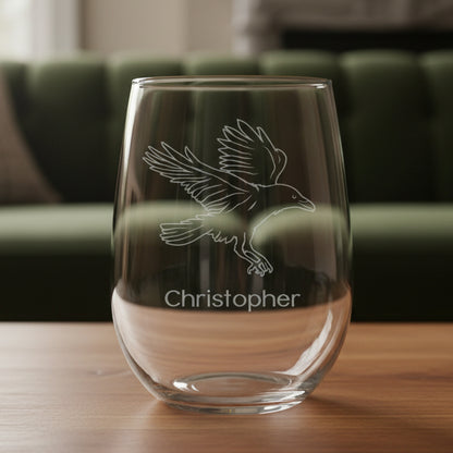 Clear glass stemless wine glass with engraved bird design and 'Christopher' text on a wooden surface.