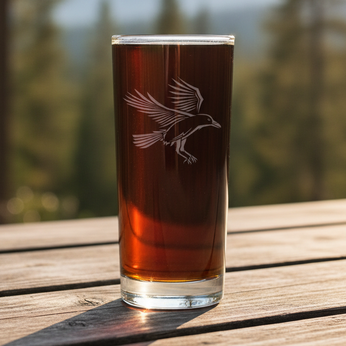 Cooler glass with a Raven etching on it with a blurred forest in the background