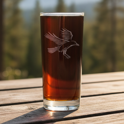 Cooler glass with a Raven etching on it with a blurred forest in the background