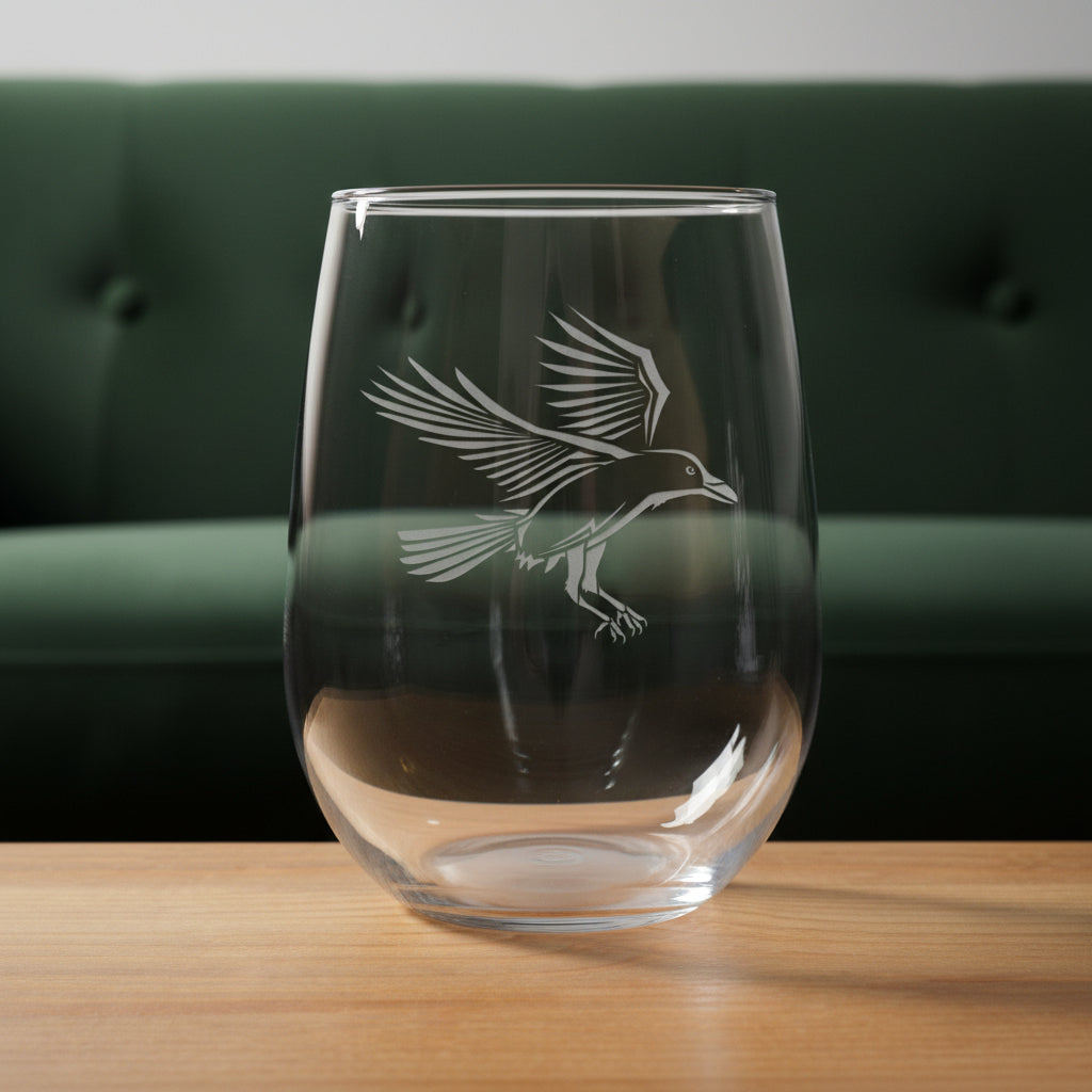 Clear glass with a bird etching on a wooden surface with a green couch in the background