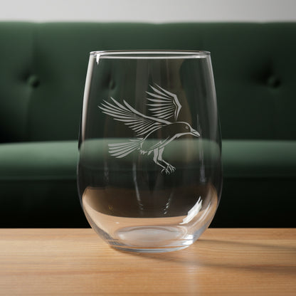 Clear glass with a bird etching on a wooden surface with a green couch in the background