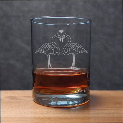 Clear glass tumbler with flamingo design filled with amber liquid on a wooden surface.