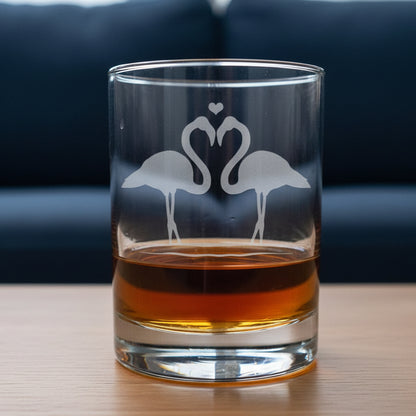 Clear glass tumbler with flamingo design filled with amber liquid on a wooden surface.