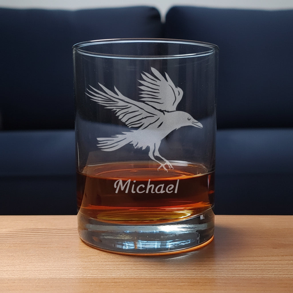 Glass tumbler with engraved bird design and 'Michael' text, filled with amber liquid on a wooden surface.
