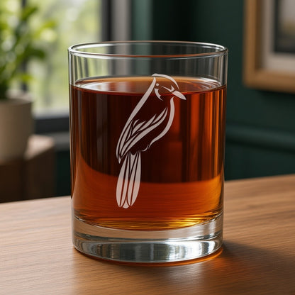 A clear rocks glass with an etched bird design, filled with Ginger ale, set on a wooden table in a softly blurred indoor setting.