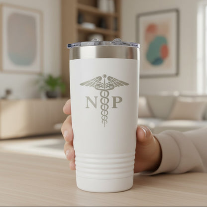 A hand holding a white insulated travel tumbler with an laser engraved  medical caduceus symbol with the letters 'NP' on the front, set against a softly blurred living room background.
