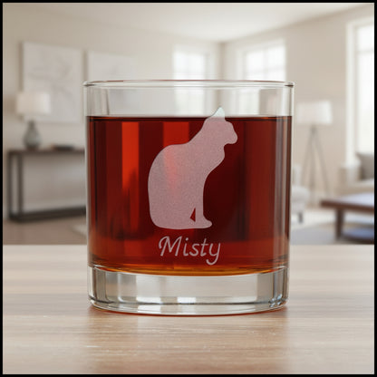 A clear glass rocks tumbler filled with an amber-red drink, featuring an etched  cat silhouette and the name 'Misty' on the front