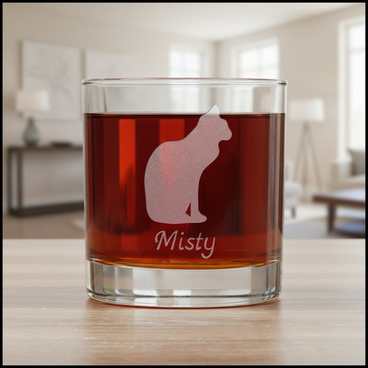 A clear glass rocks tumbler filled with an amber-red drink, featuring an etched  cat silhouette and the name 'Misty' on the front