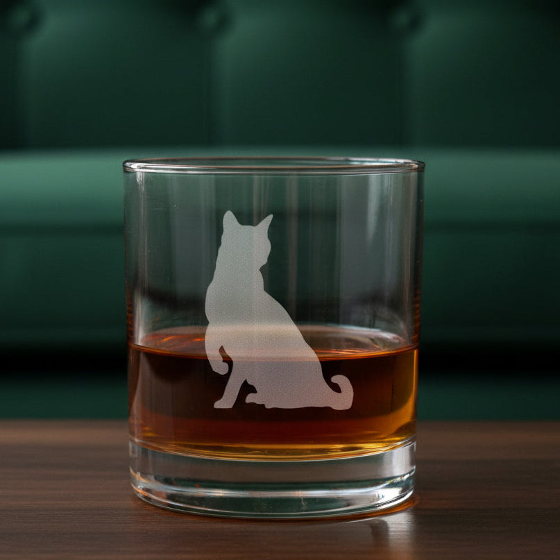 A clear rocks glass filled with amber-red liquid, featuring an etched cat silhouette 