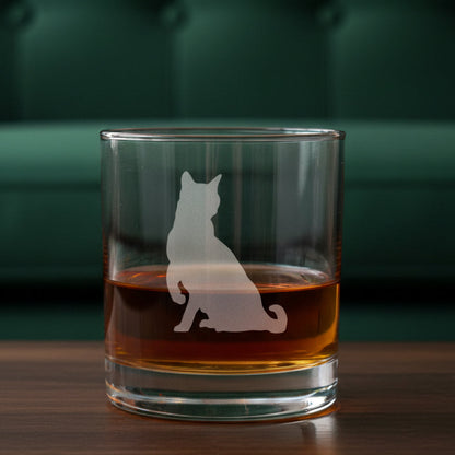A clear rocks glass filled with amber-red liquid, featuring an etched cat silhouette 