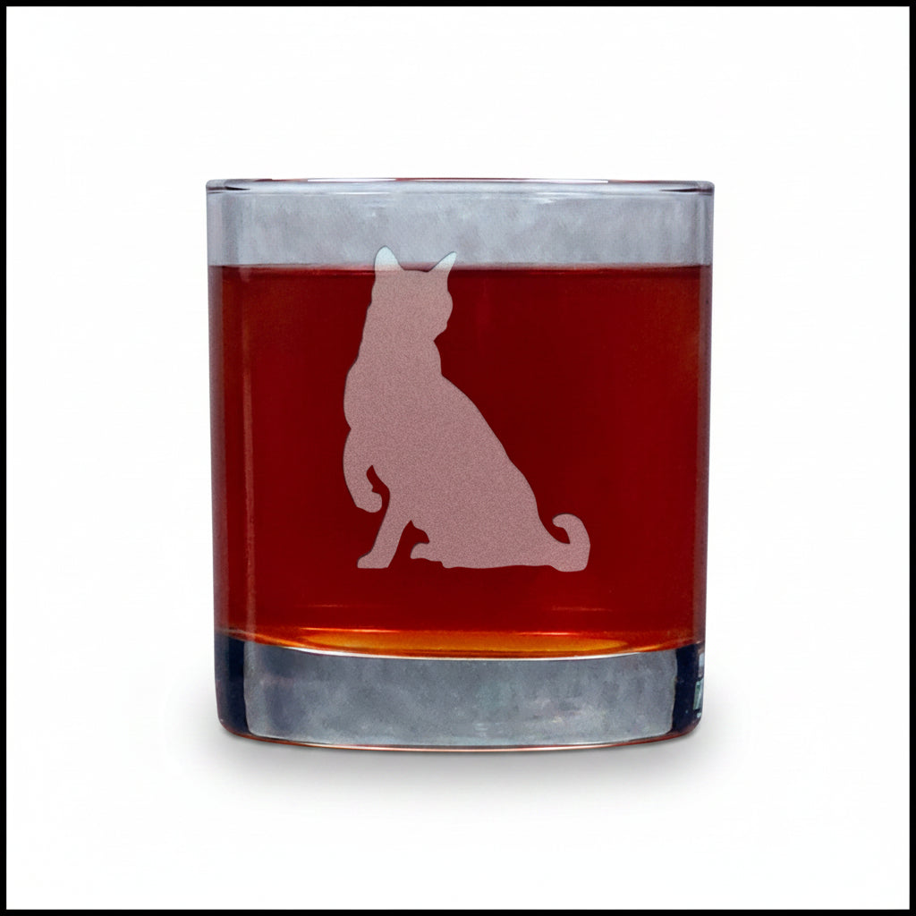A clear rocks glass filled with amber-red liquid, featuring an etched  cat silhouette on the side, set against a white background.