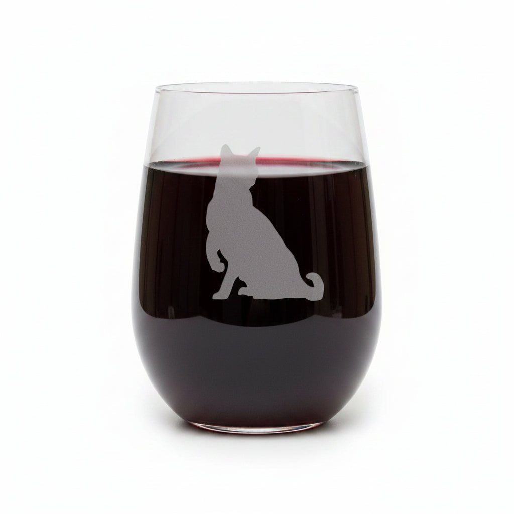 A clear stemless wine glass with a gray etched silhouette of a sitting cat, displayed on a wooden surface against a solid white background.